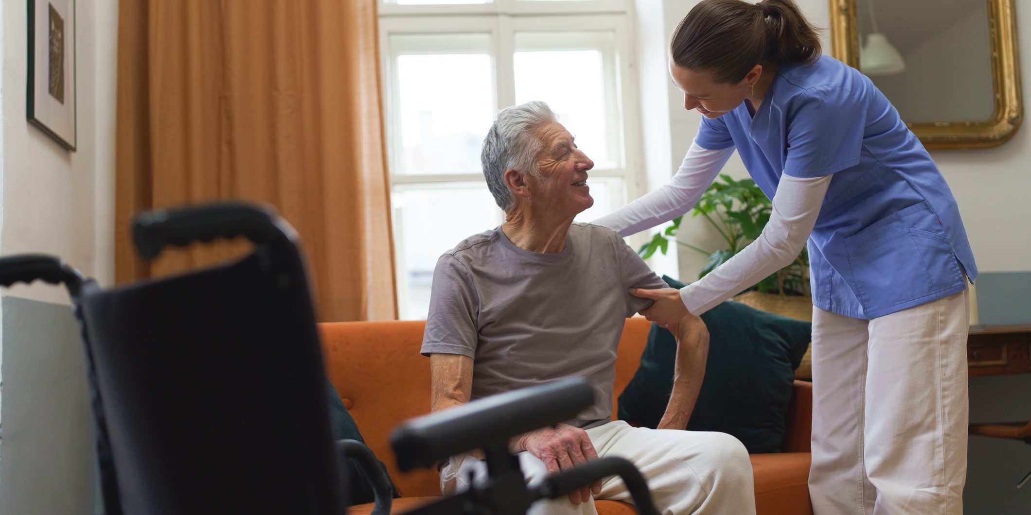 Young nurse taking care of elderly senior, helping him with walking.