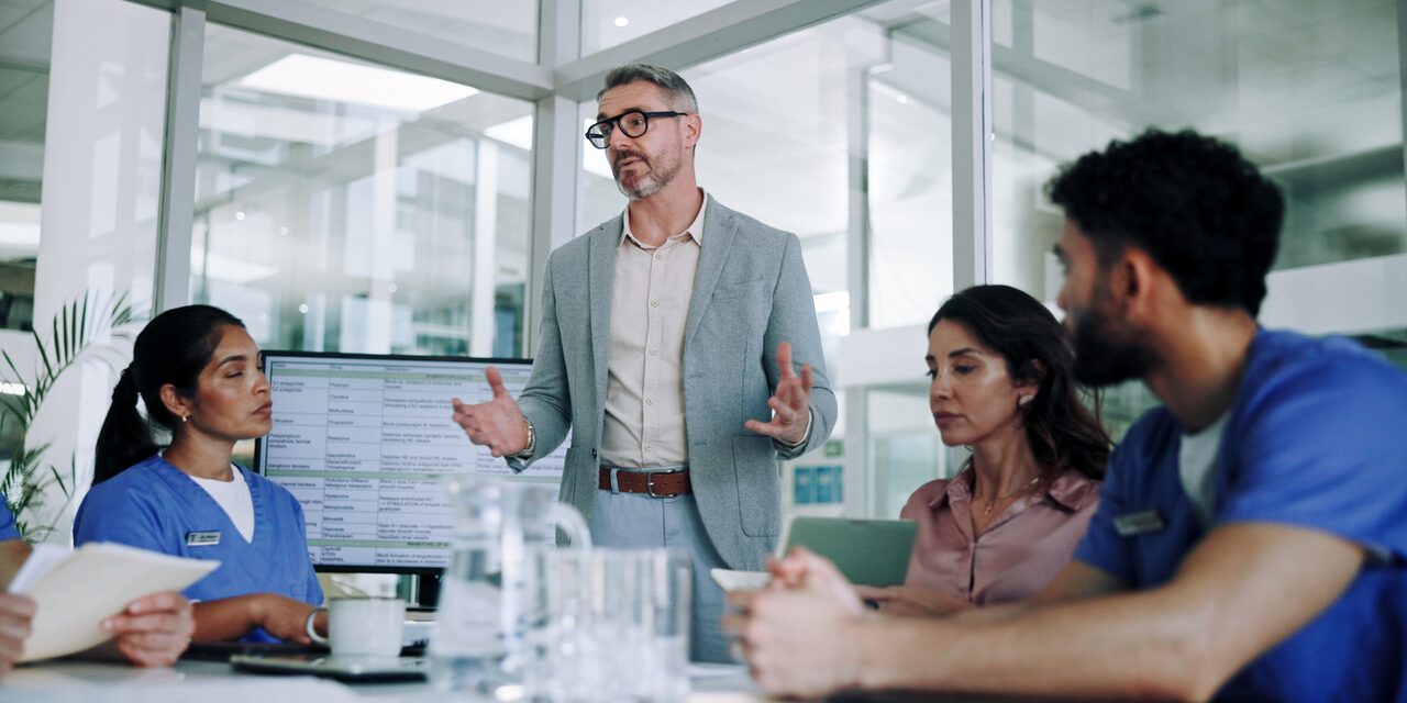 Man, medical team and meeting with presentation in conference for planning, proposal or discussion at hospital. Male person, speaker or group of healthcare employees listening to executive director